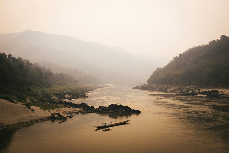 Longtail boat on the misty Mekong River at sunrise with green hills