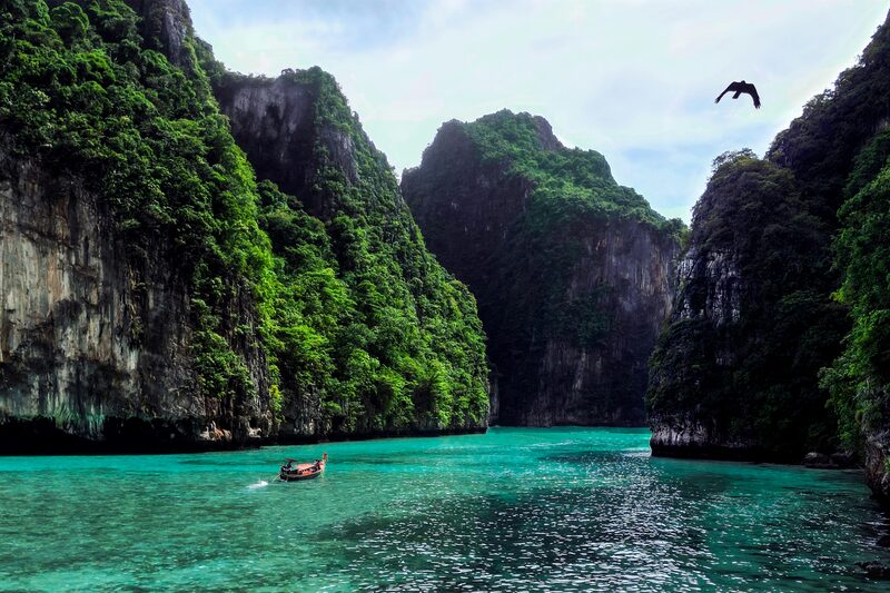 Longtail boat gliding through turquoise water between limestone cliffs at Phi Phi, Thailand