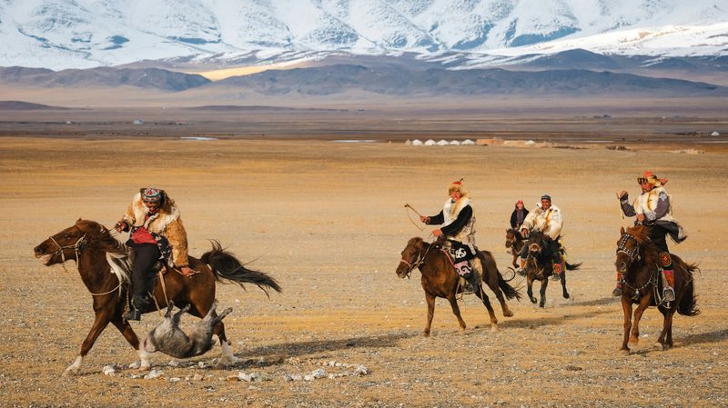 Mongolian horsemen in traditional dress playing buzkashi on the steppe