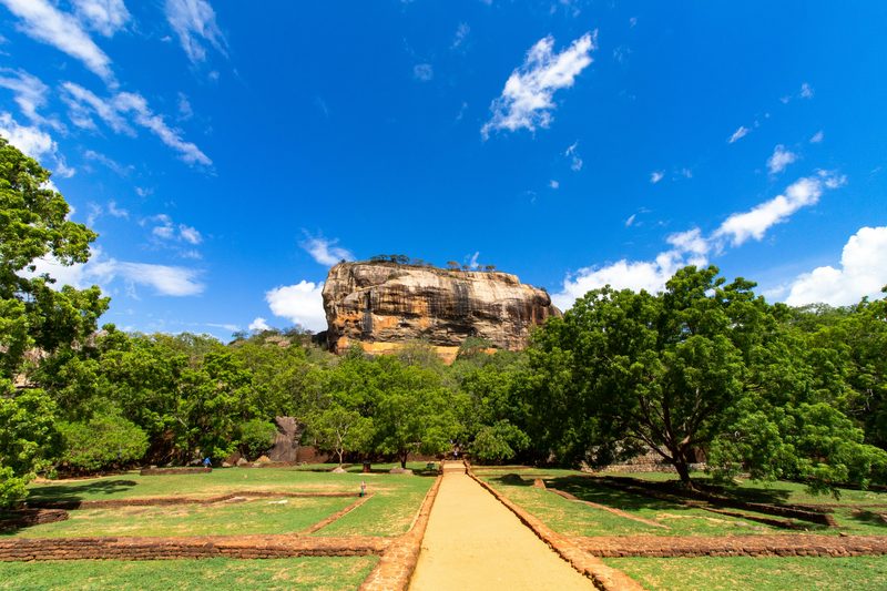 Sigiriya Rock Fortress rising above lush gardens under blue sky