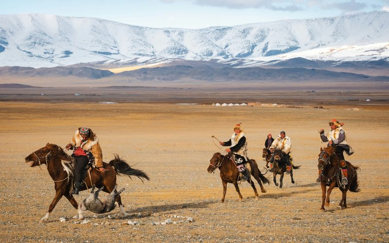 Horsemen riding across the Mongolian steppe with snow-capped mountains