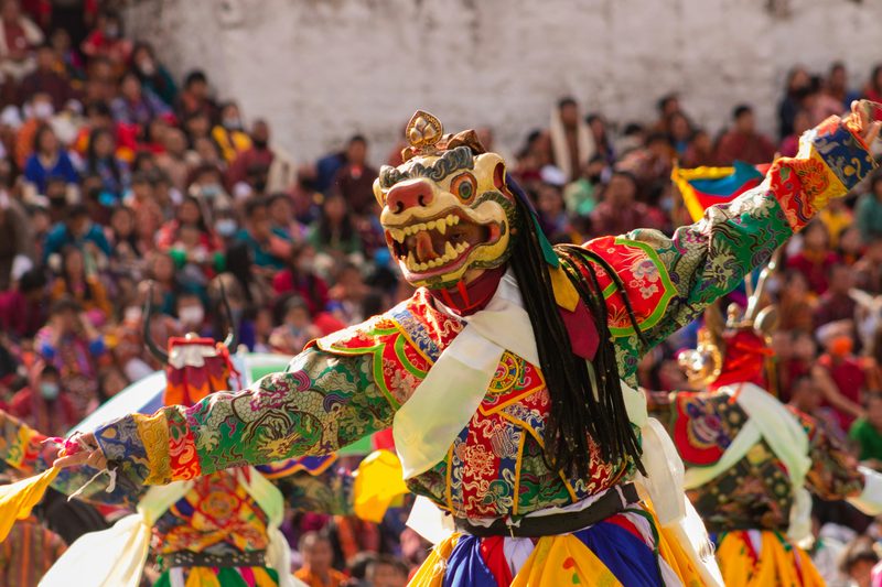 Masked dancer in colorful brocade robes performing at a Bhutanese tshechu