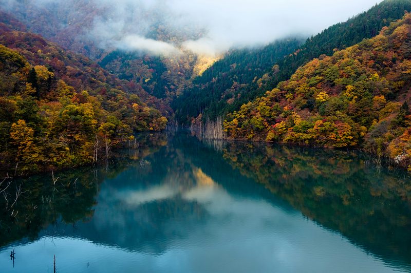 Mountain lake reflecting autumn foliage in brilliant reds and golds
