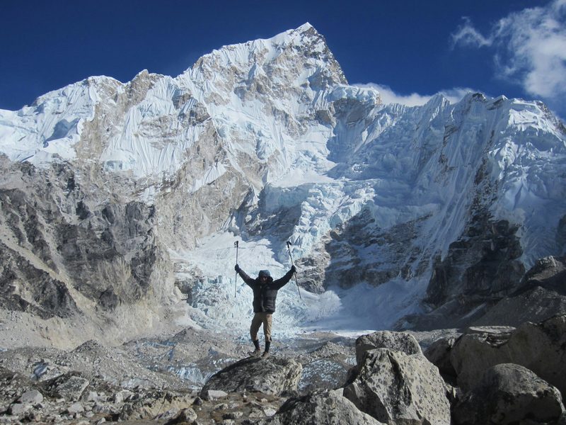 Trekker celebrating at Everest Base Camp with Himalayan peaks behind