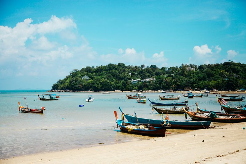 Traditional longtail boats on sandy beach with tropical island backdrop
