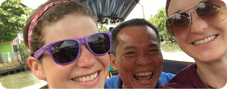 close up selfie of two sisters and one man on a small covered boat. 