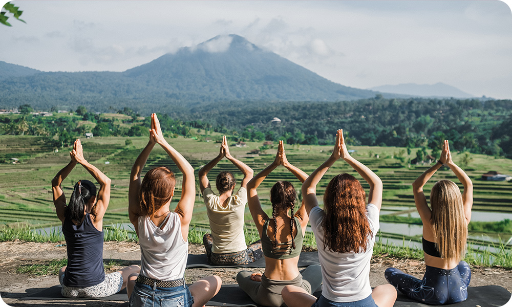 Group of female yogis in the foreground, beautiful green landscape, rice terraces in the middle, and a mountain on the back