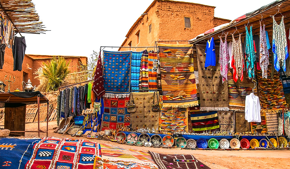 Souvenir store in Morocco. Colorful tapestry and dishes. Terracota buildings in the background